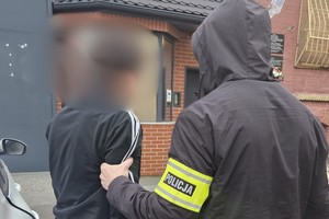 na zdjęciu policjant po cywilu z zatrzymanym przed budynkiem