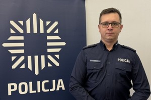 na zdjęciu dzielnicowy Jurczyk przy banerze z napisem policja