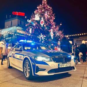 na zdjęciu radiowóz policyjny w oddali przystrojona choinka i widoczny ruch osób