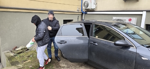 na zdjęciu widoczny policjant operacyjny wyprowadzający z radiowozu nieoznakowanego zatrzymanego mężczyznę