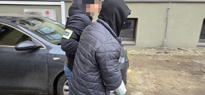 na zdjęciu widoczny policjant operacyjny prowadzący zatrzymanego mężczyznę