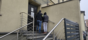 na zdjęciu widoczny policjant operacyjny prowadzący po schodach do komendy zatrzymanego mężczyznę