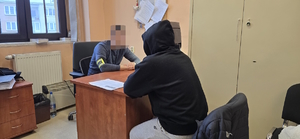 na zdjęciu widoczny policjant siedzący za biurkiem i  przesłuchujący  siedzącego przed nim zatrzymanego mężczyznę
