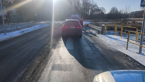 na zdjęciu samochód na jezdni, a przed nim osoby i karetka pogotowia