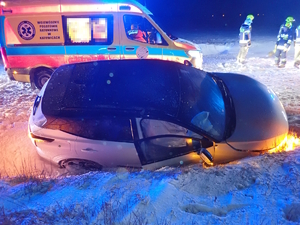 na zdjęciu biały samochód osobowy w przydrożnym, ośnieżonym rowie, po zmroku