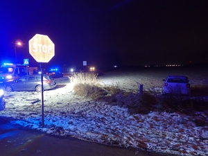 na zdjęciu po zmroku na jezdni samochód i pojazdy służb, obok na polu inny samochód