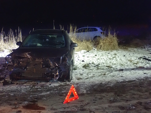 na zdjęciu ciemny samochód z rozbitym przodem, za nim na polu biały samochód po zmroku