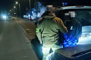 na zdjęciu policjant po cywilu z zatrzymanym mężczyzną przy samochodzie na drodze