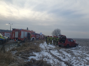 na zdjęciu rozbity samochód w polu, przy nim strażacy, obok wozy strażackie