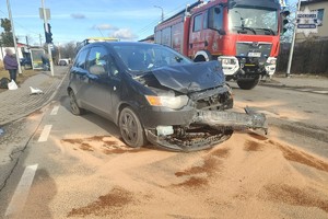 na zdjęciu czarny samochód z uszkodzeniami na jezdni, obok wóz strażacki