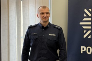 na zdjęciu policjant przy banerze w sali