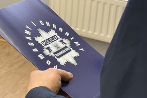 na zdjęciu dłonie policjanta trzymające teczkę z logiem policji i napisem Tarnowskie Góry