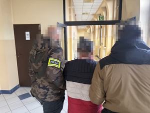 na zdjęciu policjanci prowadzą zatrzymanego