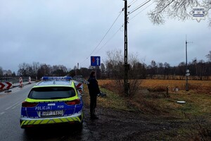 na zdjęciu policjant przy radiowozie na jezdni niedaleko rzeki