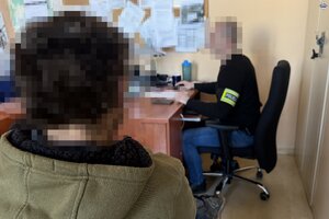 na zdjęciu policjant przy biurku, obok którego zatrzymany mężczyzna