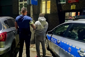 na zdjęciu policjant po cywilu z zatrzymanym przy radiowozie po zmroku