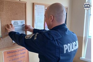 na zdjęciu policjant przywieszający ulotkę na tablicy