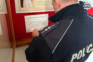 na zdjęciu policjant przywieszający ulotkę na tablicy