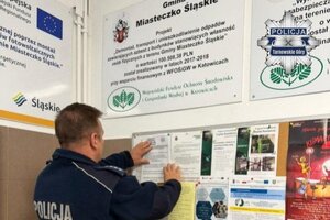na zdjęciu policjant przywieszający na tablicy ulotkę