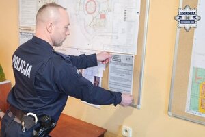 na zdjęciu policjant przywieszający ulotkę na tablicy informacyjnej