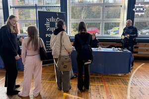 na zdjęciu stoisko policyjne, przy którym stoją osoby, policjant i uczennice w mundurach