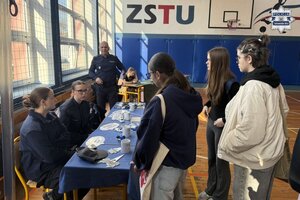 na zdjęciu stoisko policyjne, przy którym stoją osoby, policjant i uczennice w mundurach