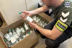 na zdjęciu policjant po cywilu a przed nim karton z butelkami z alkoholem