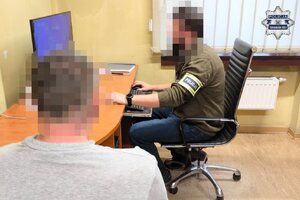 na zdjęciu policjant przy biurko, obok zatrzymany mężczyzna