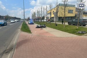 na zdjęciu leżący na chodniku motocykl, za nim radiowóz obok osoby i inne pojazdy