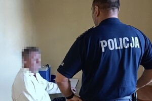 na zdjęciu policjant, a obok niego siedzący na krześle mężczyzna
