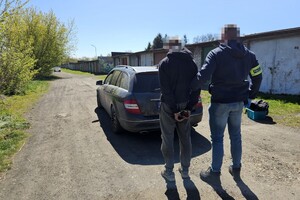 na zdjęciu policjant z opaską, obok zatrzymany, przed nimi samochód