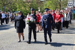 na zdjęciu od lewej funkcjonariuszka Straży Miejskiej, Strażak i Policjant jako delegacja kwiatowa