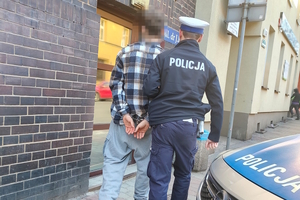 na zdjęciu policjant prowadzący zatrzymanego do budynku komendy