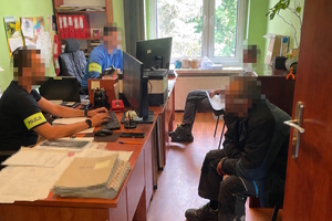 na zdjęciu policjanci w pomieszczeniu siedzący za biurkami, a przed nimi mężczyźni