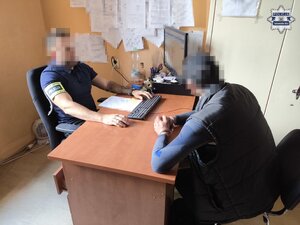 na zdjęciu zatrzymany przy biurku, za którym siedzi policjant