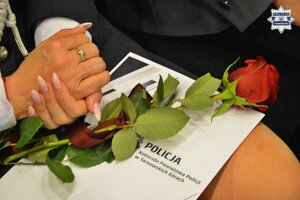 na zdjęciu dłonie kobiety, róża i teczka okolicznościowa z napisem komenda powiatowa policji w tarnowskich górach