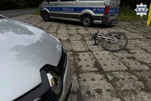 na zdjęciu fragment pojazdu, za nim leżący rower i radiowóz