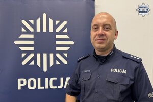 na zdjęciu dzielnicowy Golicz przy niebieskim banerze z napisem policja