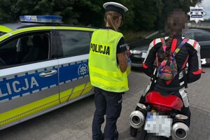 na zdjęciu policjantka, obok niej radiowóz i kierujący motocyklem w trakcie kontroli