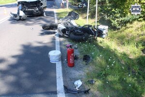 na zdjęciu motocykl leżący na jezdni i poboczu, przed nim rozbity samochód