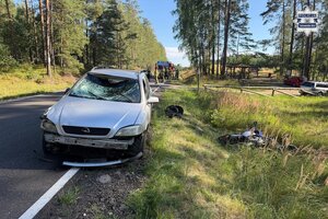 na zdjęciu samochód z uszkodzeniami na jezdni, obok w rowie motocykl, za pojazdem wóz strażacki, strażacy i policjantki