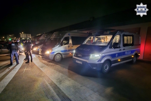 na zdjęciu radiowozy po zmroku na parkingu, obok policjanci