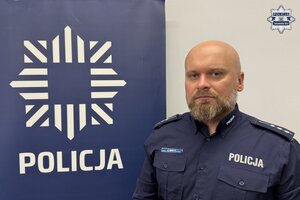 na zdjęciu dzielnicowy Bawecki przy banerze z napisem policja