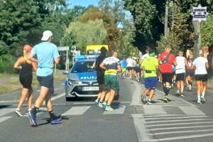 na zdjęciu radiowóz na jezdni i obok biegacze