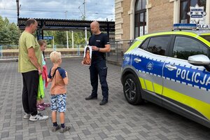 na zdjęciu policjant przy radiowozie z uczestnikami gry miejskiej