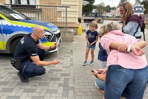 na zdjęciu policjant przy radiowozie z uczestnikami gry miejskiej
