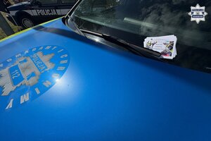 na zdjęciu fragment maski radiowozu i za wycieraczką ulotki