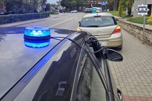 na zdjęciu lampa błyskowa z radiowozu, a przed nią na chodniku zaparkowany samochód