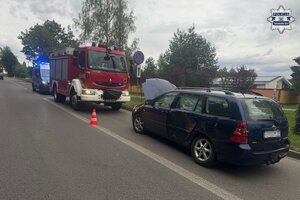 na zdjęciu uszkodzony pojazd na jezdni, przed nim wóz strażacki i radiowóz policyjny
