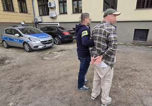 na zdjęciu policjant prowadzący do komendy zatrzymanego